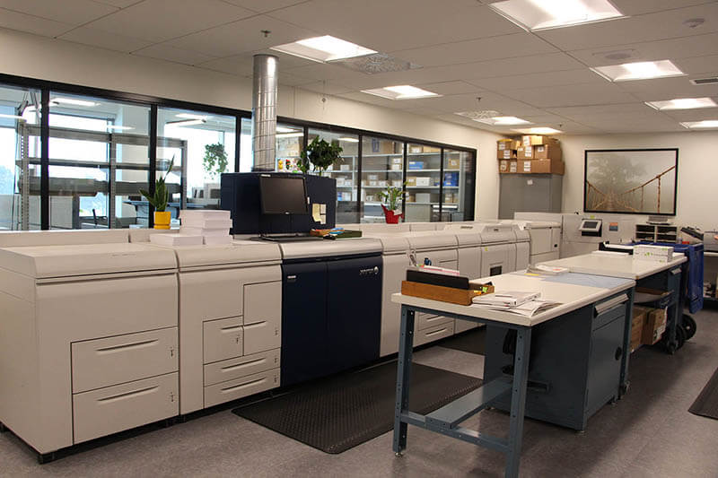 Salle de la reprographie avec plusieurs machines professionnelles pour imprimer du matériel et tables de travail.