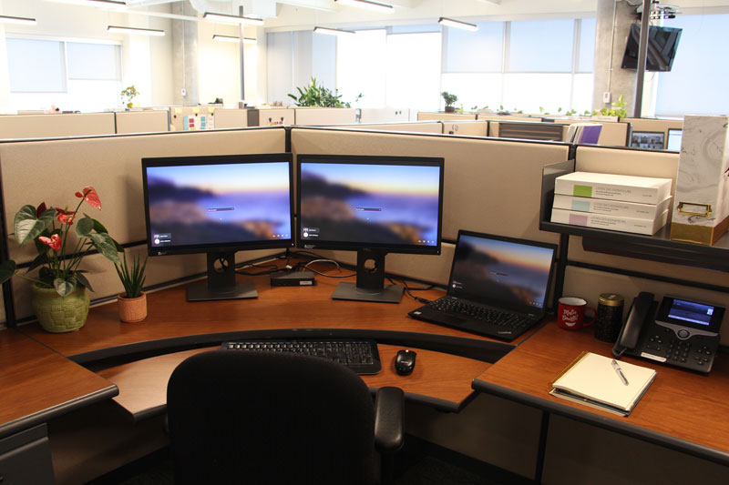 Espace de travail avec chaise, bureau, téléphone, écran, classeur et paravents pour délimiter l’espace.