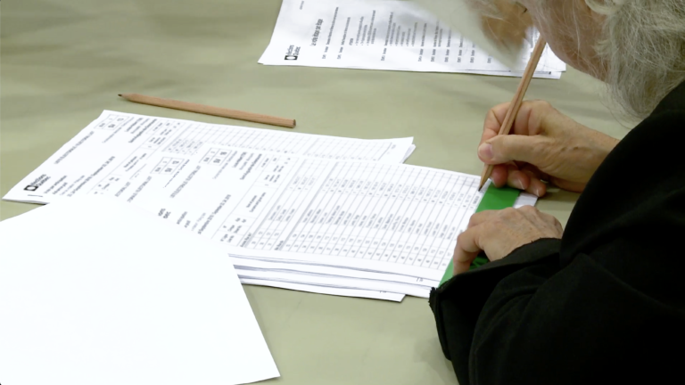 Gros plan d’un membre du personnel qui raye un nom sur la liste électorale avec un crayon de plomb et une règle.